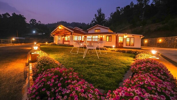 A two-story house with a well-lit lawn, a dining area with chairs, and a stone wall. - Lauriston Villa Ooty by VOYE HOMES (Ooty)
