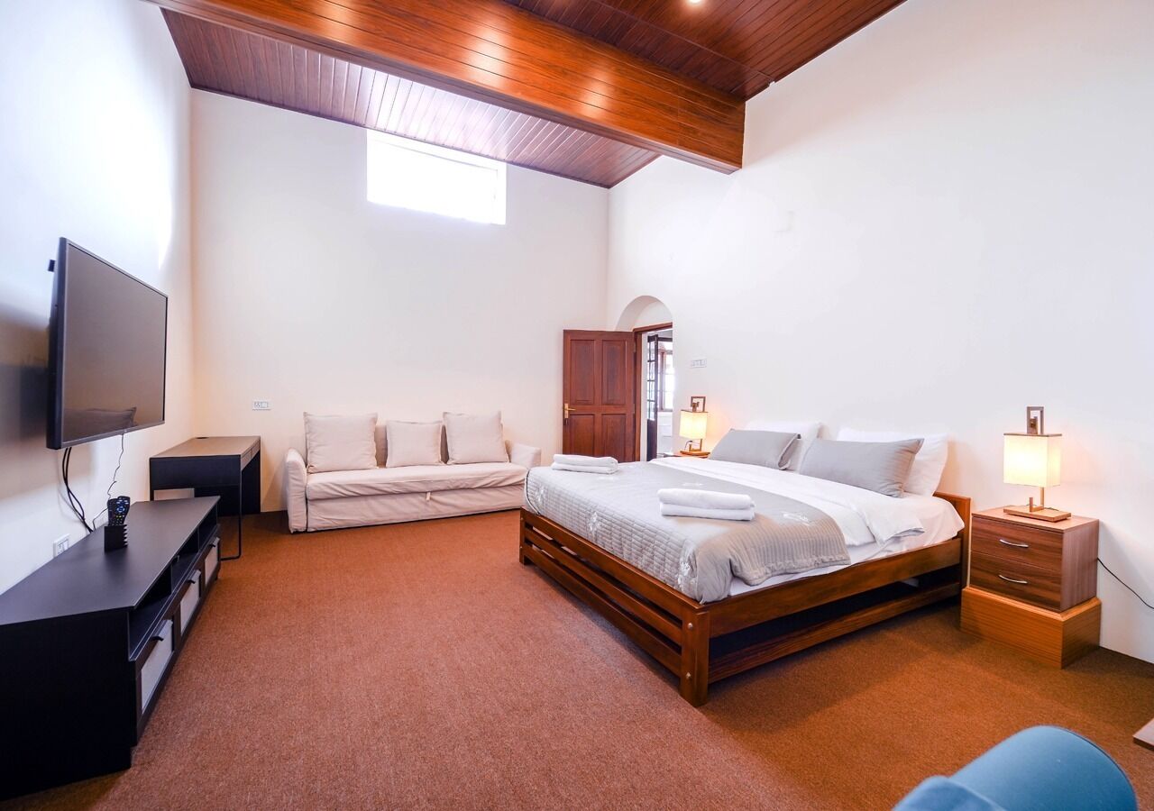 Un dormitorio con una cama, televisión, escritorio, silla y lámpara.