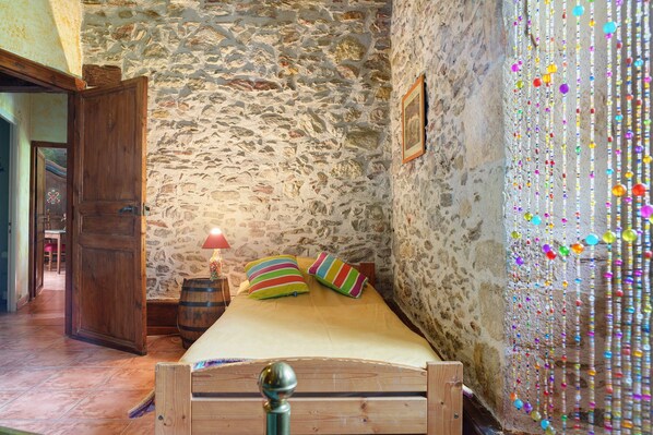 A room with a stone wall, wooden bed, colorful pillows, and a decorative curtain.