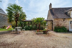 Un edificio de piedra con un patio de grava, mobiliario exterior y una palmera.