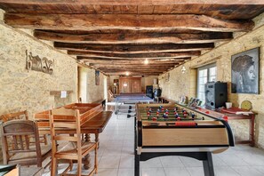 Una habitación con mesa de fútbol de mesa, sillas de madera, paredes de piedra y techo de madera.