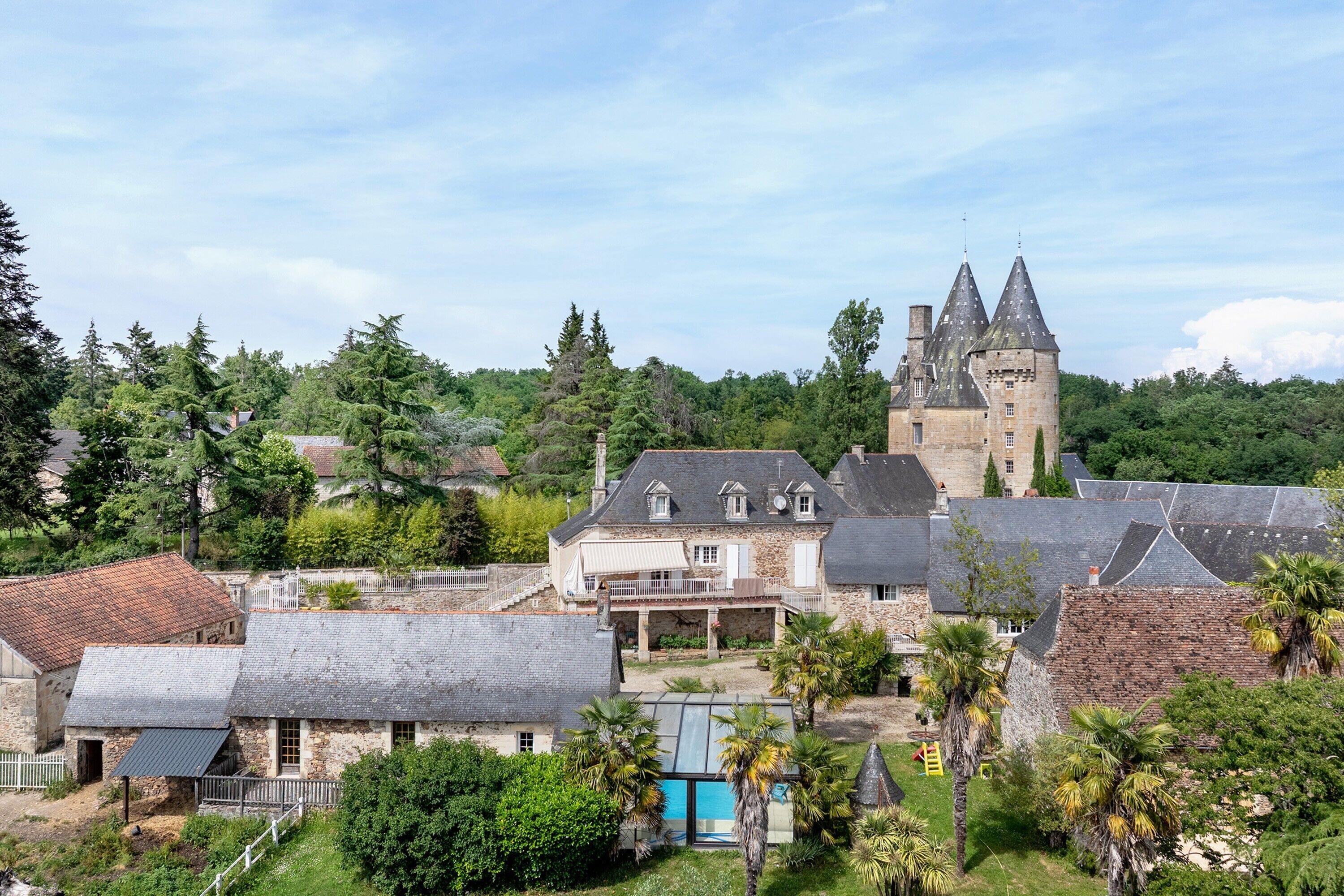 A castle with a tower, surrounded by trees and a swimming pool.