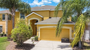 A yellow two-story house with a garage, surrounded by palm trees and a well-maintained lawn. - Pvt Pool&Spa·Game Room·BBQ·Near Theme Parks (Kissimmee)