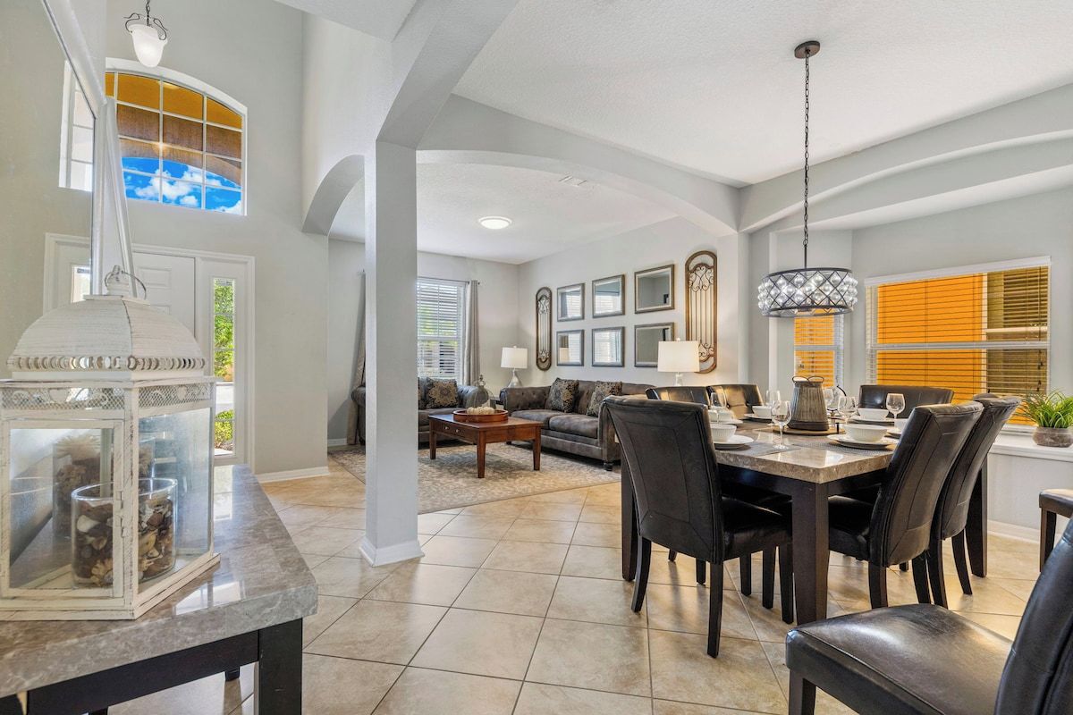 A spacious living area with a dining table set for six, a sofa, and a chandelier.