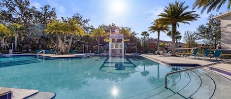 A swimming pool with a water slide, surrounded by palm trees and lounge chairs.