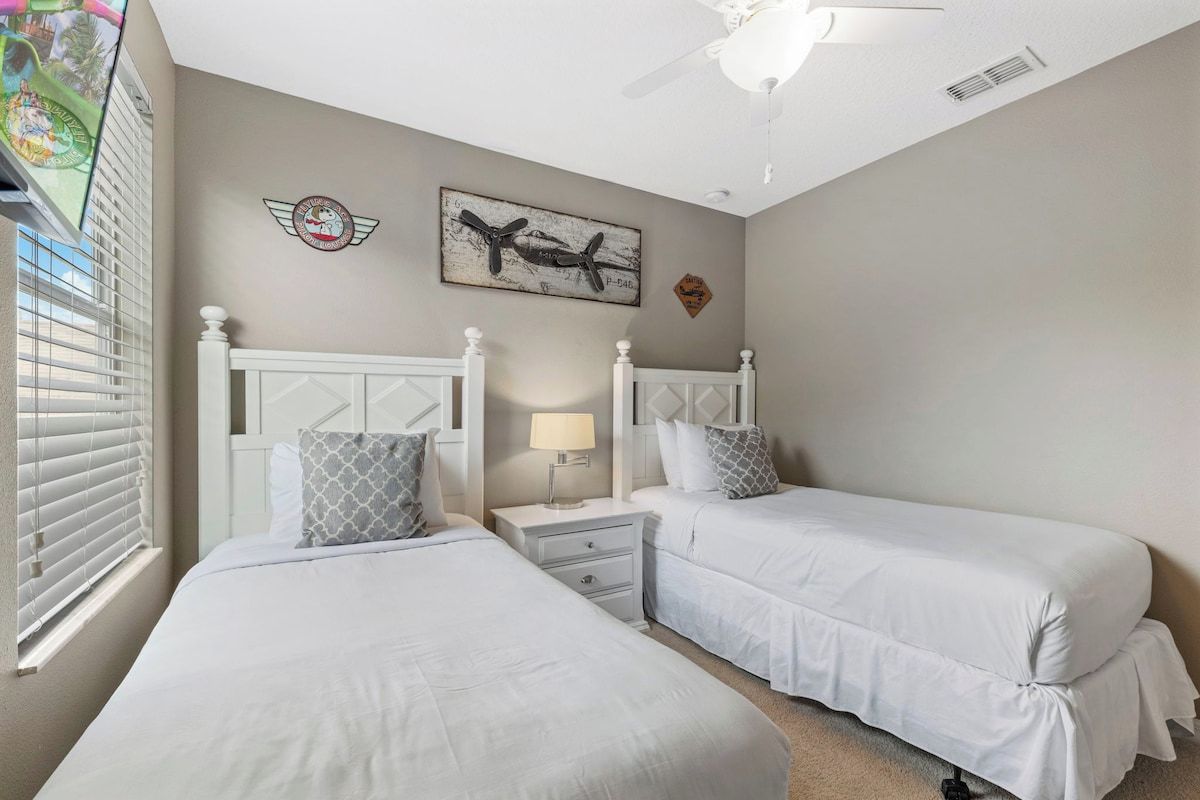 A bedroom with two beds, a ceiling fan, a nightstand, and a wall-mounted airplane picture.