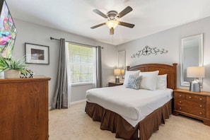 A bedroom with a bed, a ceiling fan, a nightstand with lamps, a dresser, a window with curtains, and a wall decoration. - Pvt Pool&Spa·Game Room·BBQ·Near Theme Parks (Kissimmee)