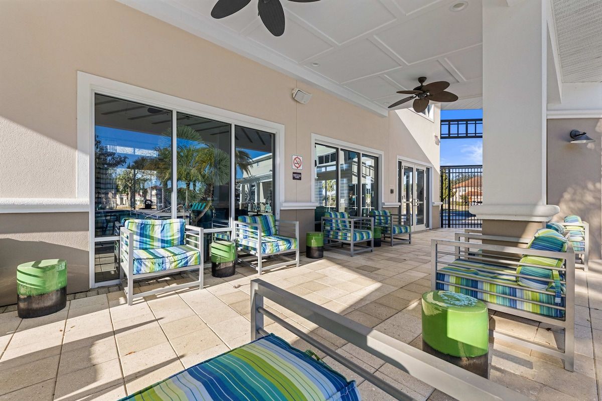 A covered outdoor seating area with multiple chairs and tables, a ceiling fan, and a view of the surrounding buildings.
