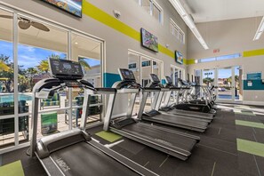 Ein Fitnessstudio mit Laufbändern, Trainingsgeräten und großen Fenstern mit Blick ins Freie.