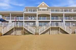 Ein mehrstöckiges Strandhotel mit Balkonen, ein Sandstrand davor und ein klarer Himmel.