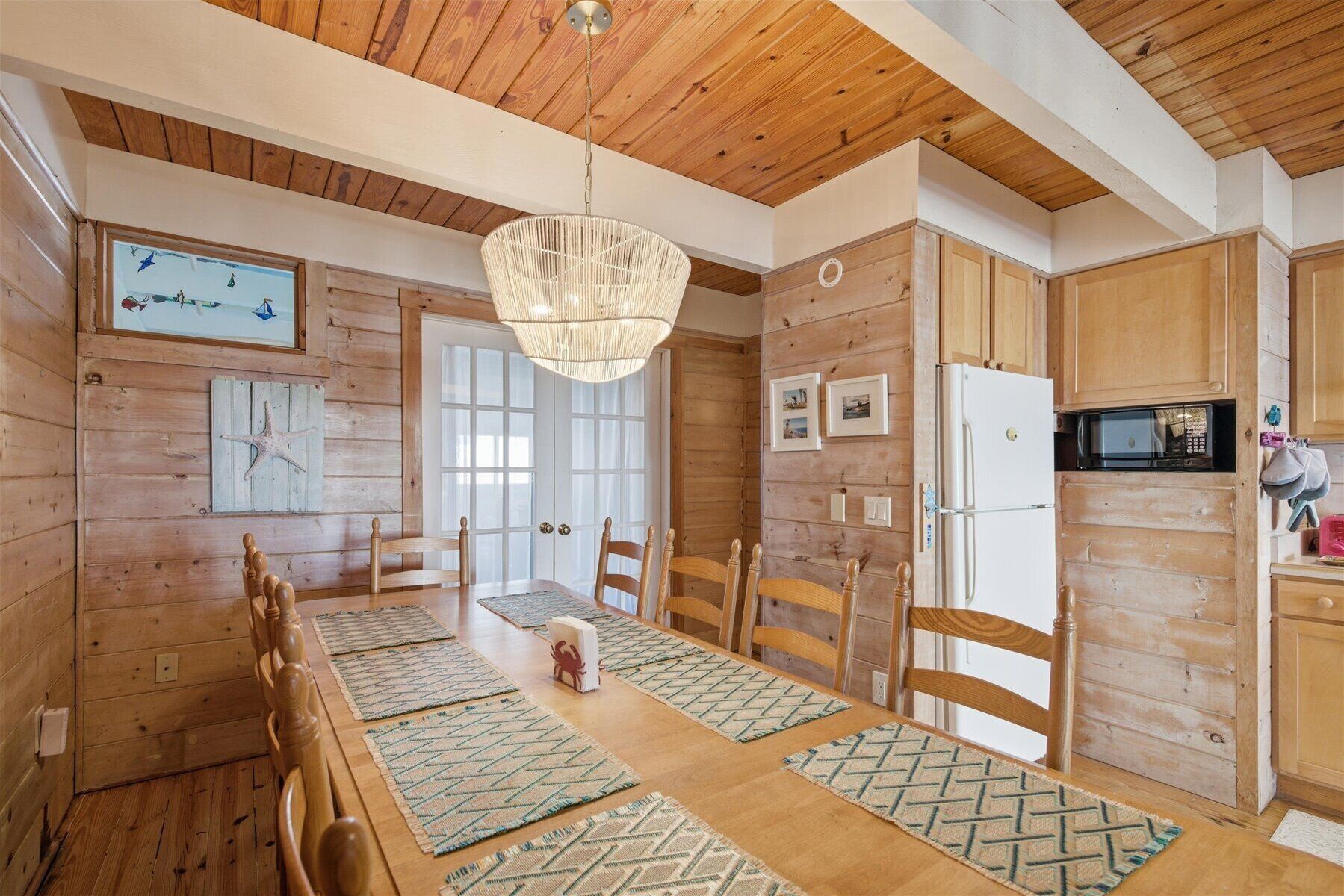 A wooden interior with a dining table, chairs, a hanging light fixture, and a kitchen area with appliances.