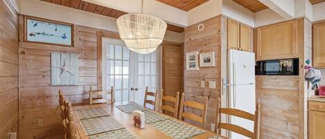 A wooden interior with a dining table, chairs, a hanging light fixture, and a kitchen area with appliances.