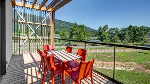 A wooden deck with a table and chairs, a glass railing, and a view of a lake and trees. - Stay With Terrace Near the Rhone (Motz)