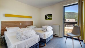 A hotel room with two beds, a chair, a radiator, and a window with a view of a building and hills. - Stay With Terrace Near the Rhone (Motz)