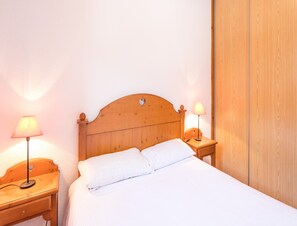 A neatly made bed with white linens, two bedside tables with lamps, and a wooden wardrobe. - Attractive Apartment With Balcony/terrace (Modane)
