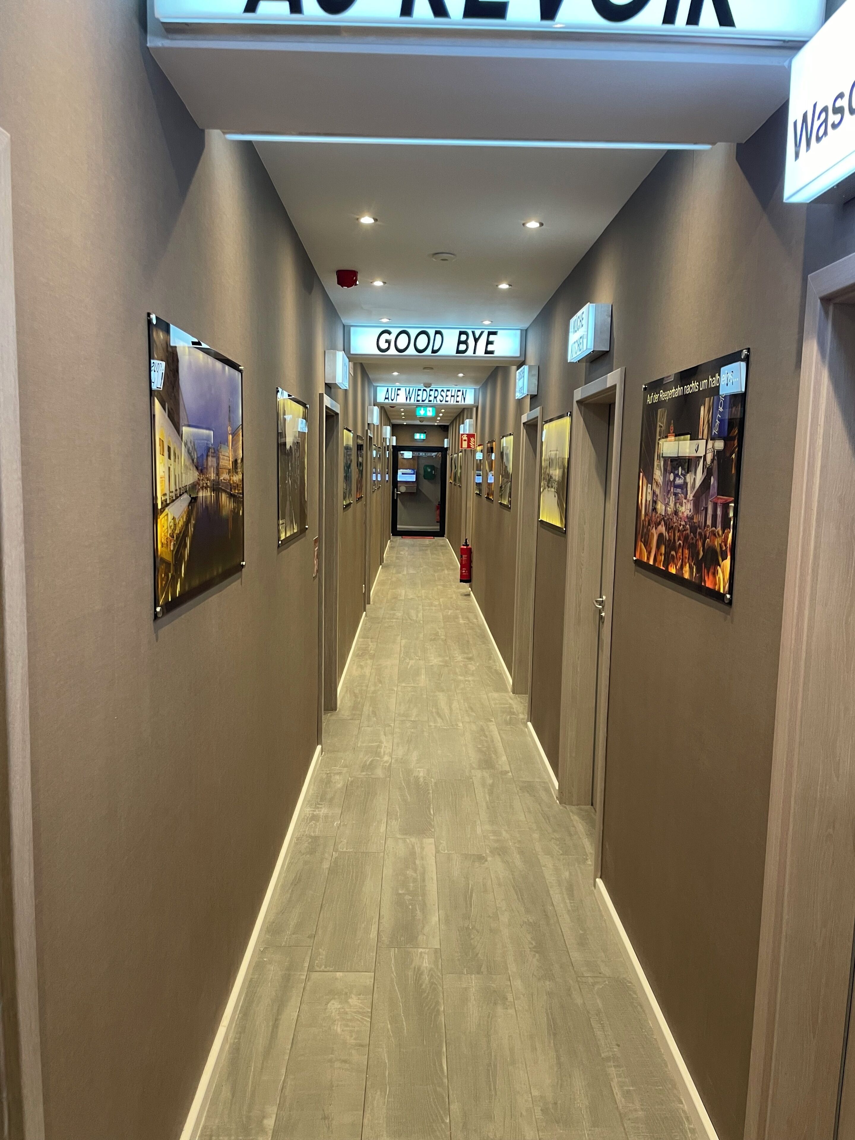 A hotel hallway with a 'GOOD BYE' sign, 'AUF WIEDERSEHEN' sign, and a 'Was' sign.