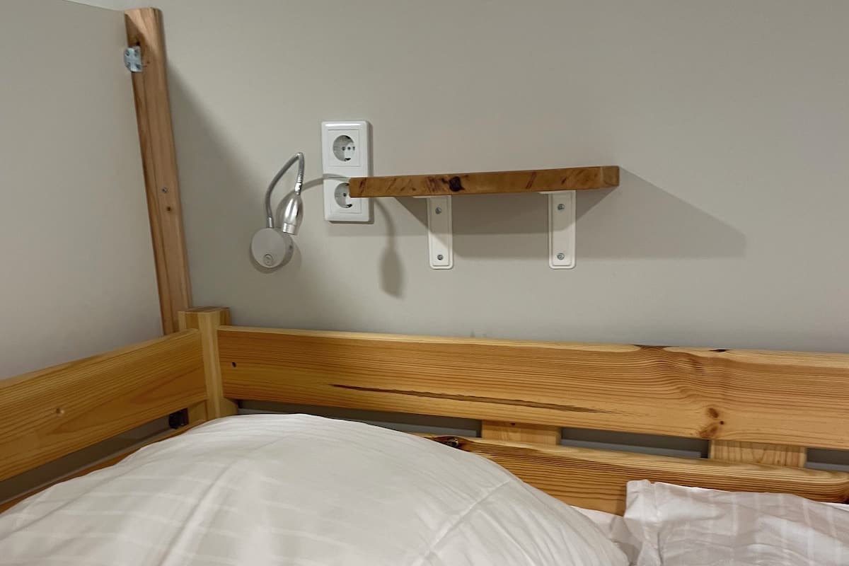 A wooden bunk bed with white bedding, a wall-mounted shelf, and a power outlet.