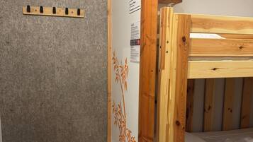 Una cama litera con estructura de madera y ropa de cama blanca, una pared gris con textura y una puerta decorada con motivos de bambú.