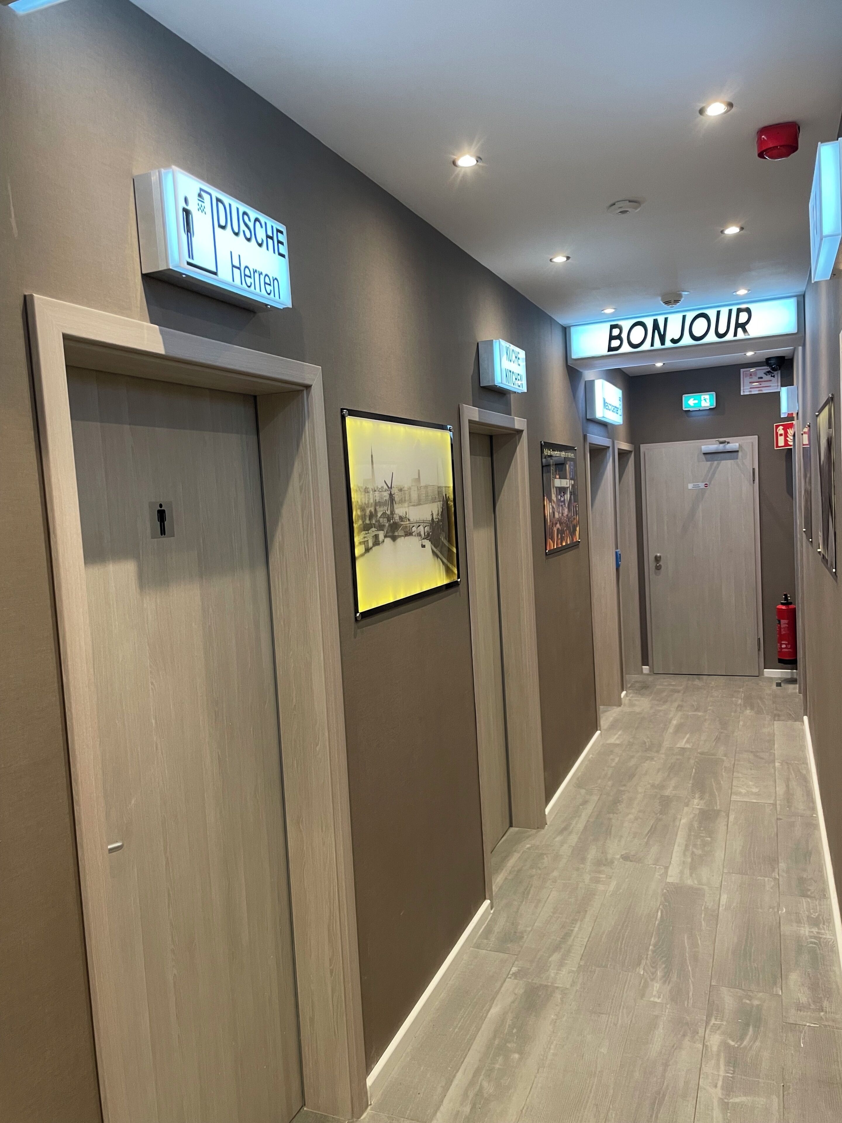 Un pasillo de hotel con puertas de madera, un cartel de bienvenida y un letrero que indica el baño de hombres.