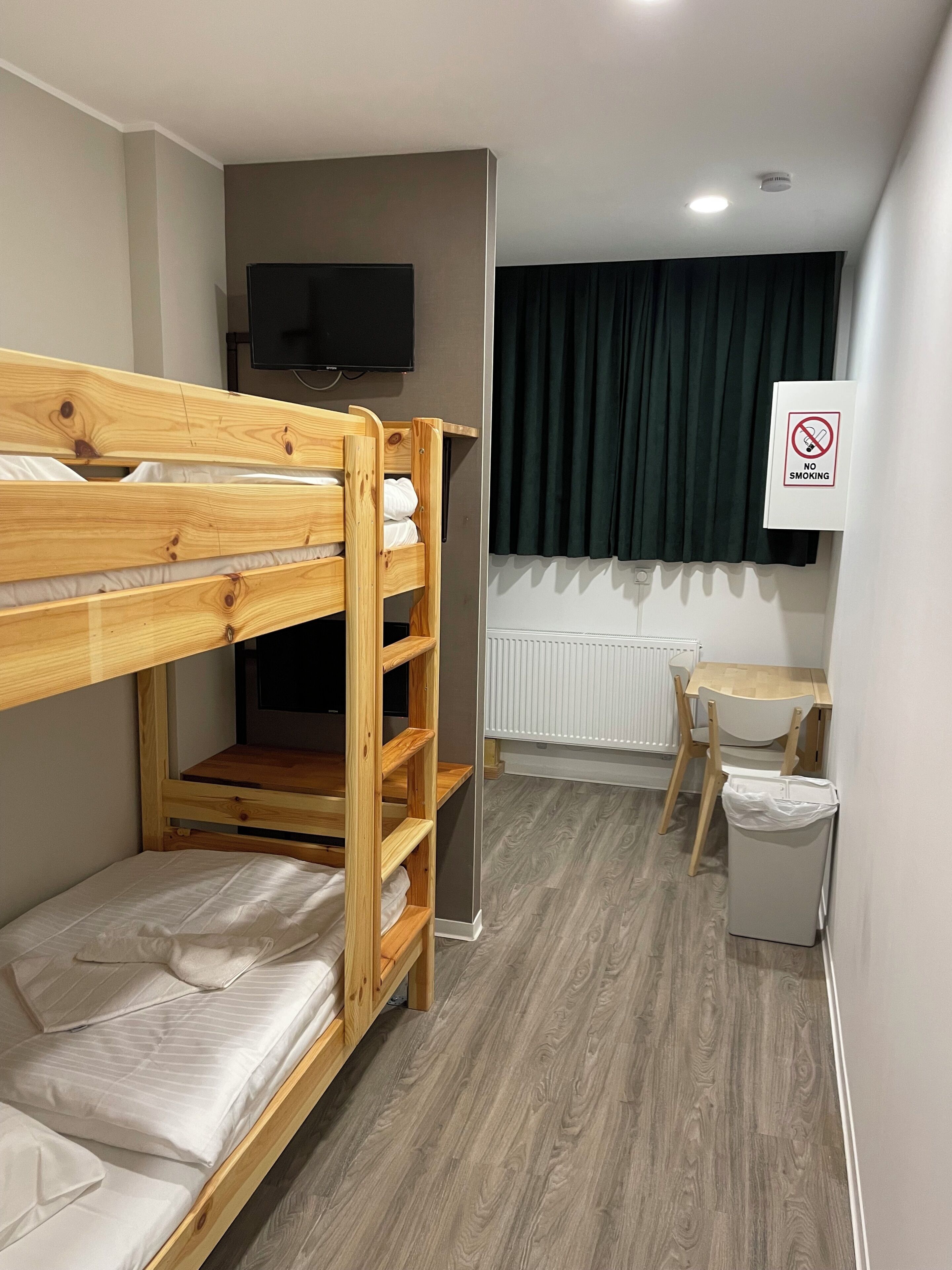 A bunk bed with a TV above it, a desk with a chair, a radiator, and a 'No Smoking' sign.