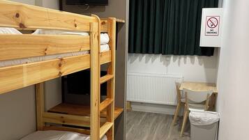 A bunk bed with a TV above it, a desk with a chair, a radiator, and a 'No Smoking' sign.