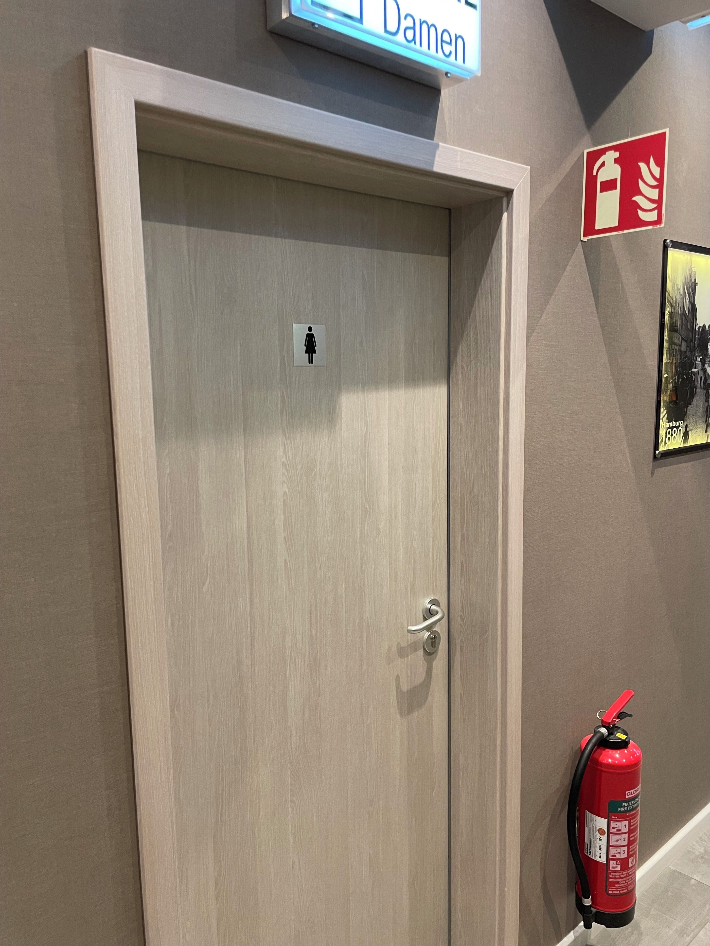 Una puerta de madera con el símbolo de baño de mujeres, un extintor y un cartel que indica 'Damen' baños.