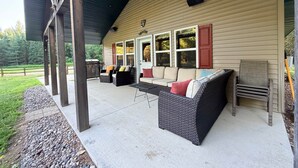 Une terrasse couverte, aménagée avec du mobilier d’extérieur, un barbecue et offrant une vue sur le paysage environnant.