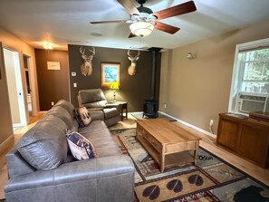 A living room with a sofa, a coffee table, a fireplace, and a ceiling fan. - Upper Peninsula Peaceful Cabin (Nadeau Township)