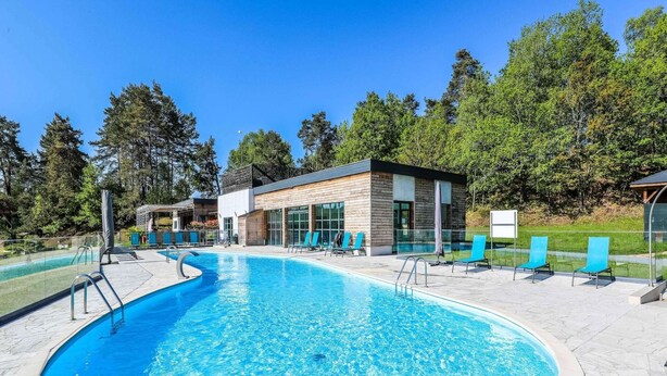 En swimmingpool med liggestole, en moderne bygning og en klar himmel.