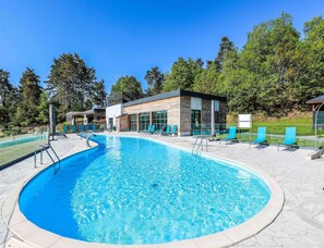 Une piscine avec des chaises longues, un bâtiment moderne et un ciel dégagé.