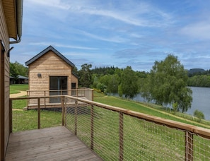 Une cabane en bois dotée d’un balcon donnant sur un lac, le tout entouré de verdure.