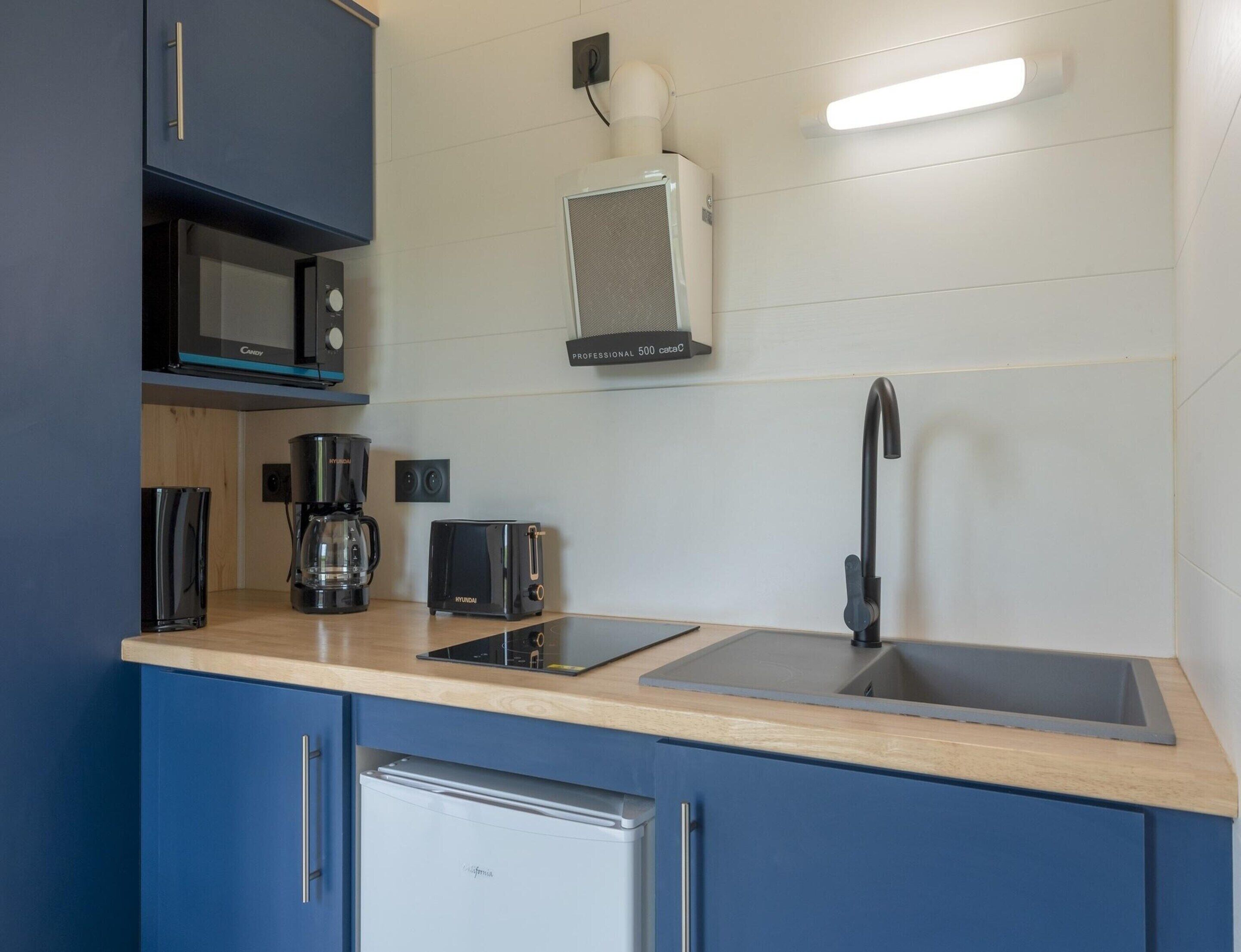A modern kitchen with a microwave, toaster, coffee maker, sink, and a small refrigerator.