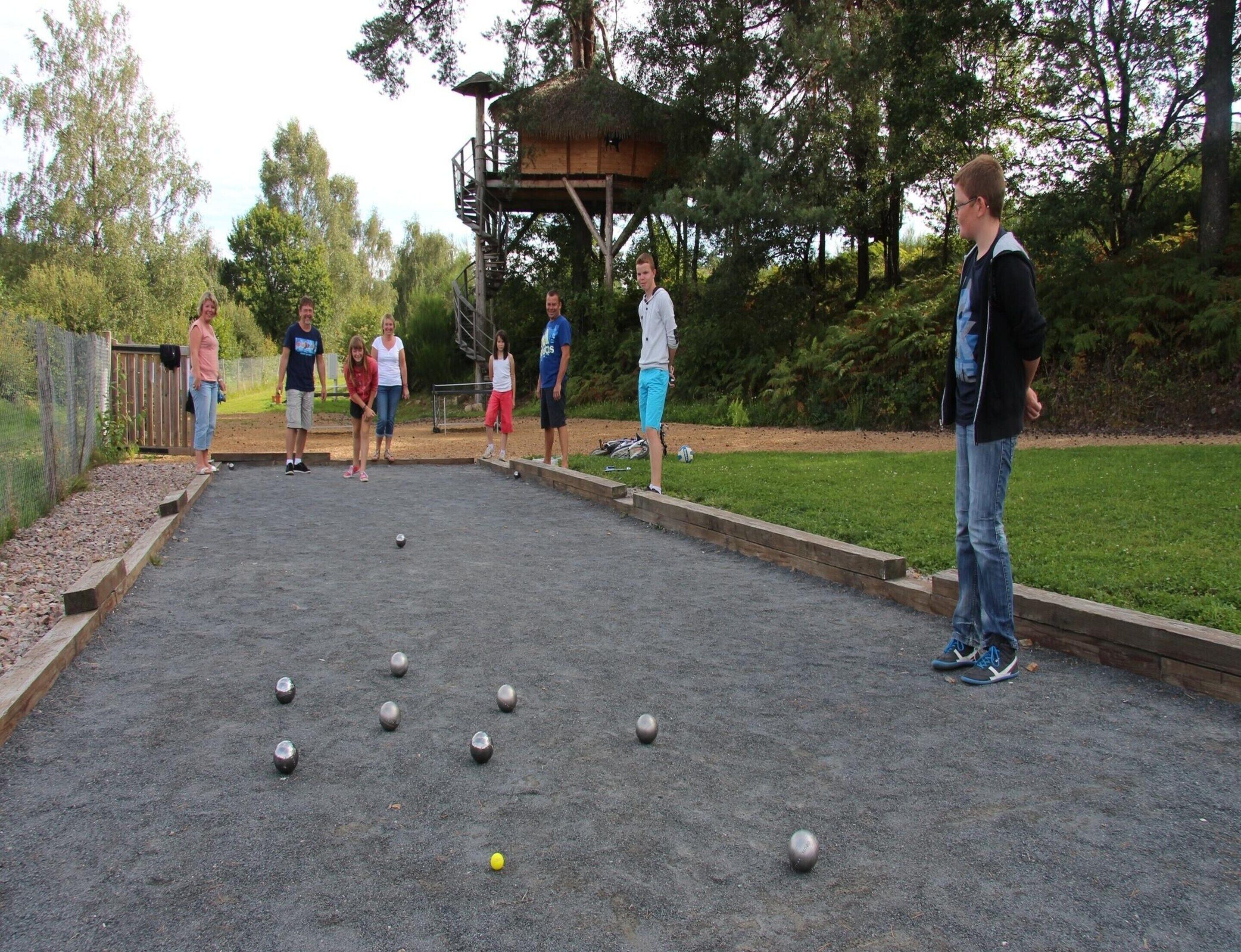 A group of people playing a game on a gravel court with a wooden structure in the background.