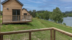 En træhytte med balkon, hegnede terrasse og udsigt til sø og skov.
