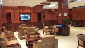Un vestíbulo de hotel con sofás de cuero, un televisor, una recepción y una planta decorativa.