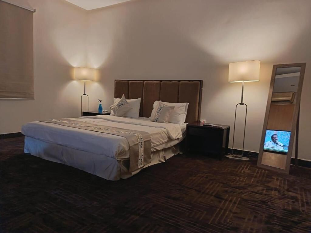 A hotel room with a large bed, two bedside lamps, a TV, and a wooden floor.