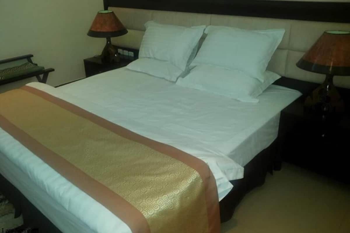 Una cama bien hecha con una colcha estampada, dos lámparas de noche y una mesita de noche con lámpara.
