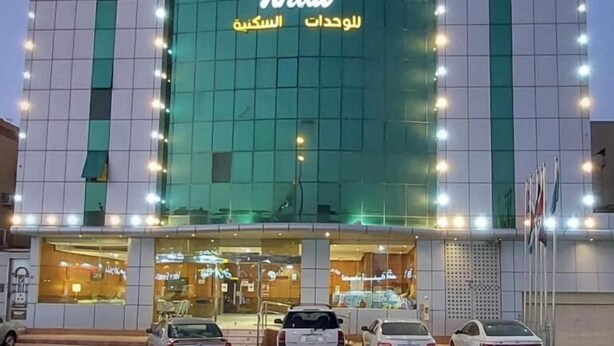 Un edificio con un cartel iluminado grande que dice 'Khal' y texto en árabe debajo. Hay varios coches estacionados adelante.