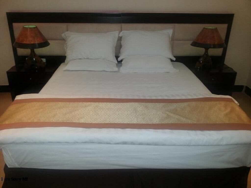A bed with white bedding, two bedside lamps, and a dark headboard.