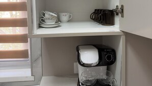 Keittiössä on kahvinkeitin, mikroaaltouuni ja kaappi, jossa on hyllyjä.