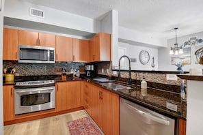 Cocina con armarios de madera, electrodomésticos de acero inoxidable, encimeras de granito, un lavamanos y salpicadero.
