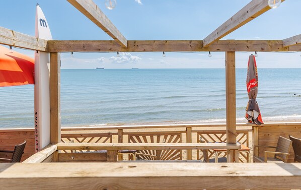 A wooden beach bar with a view of the sea, featuring a simple seating arrangement and a flag.