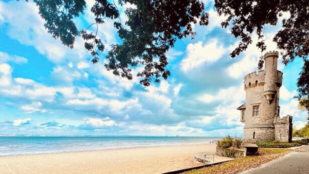 A beach with a stone tower, a paved walkway, and a clear sky. - Sandlands (Ryde)