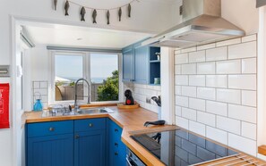 A modern kitchen with blue cabinets, a stainless steel sink, and a view of the sea.