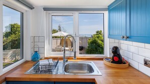 A modern kitchen with a large window, a dish rack, a coffee machine, and a view of the outdoors. - Red Cedars (Bembridge)