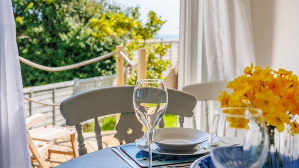 A table set with a wine glass, a plate, and a vase with yellow flowers. - Red Cedars (Bembridge)