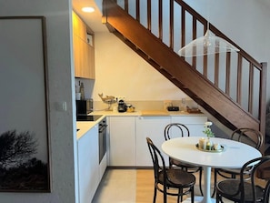 Eine moderne Küche mit weißen Schränken, einer Holztreppe und einem Essbereich mit rundem Tisch und Stühlen.