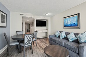 Ein Wohnzimmer mit grauem Sofa, einem runden Couchtisch und einem an der Wand montierten Fernseher.