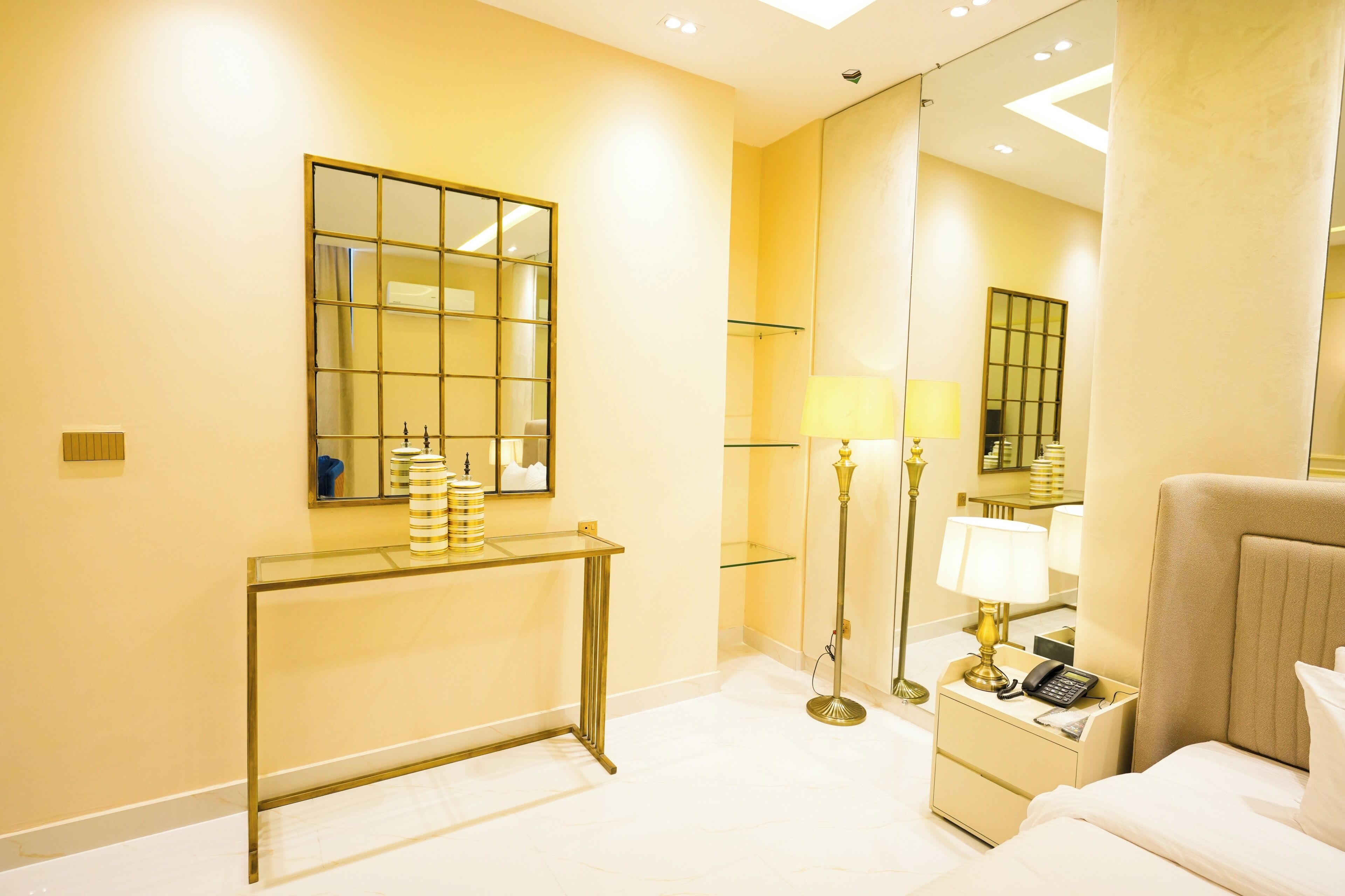 Une chambre d’hôtel comprenant un lit, une table de chevet, une lampe, une commode et un grand miroir.