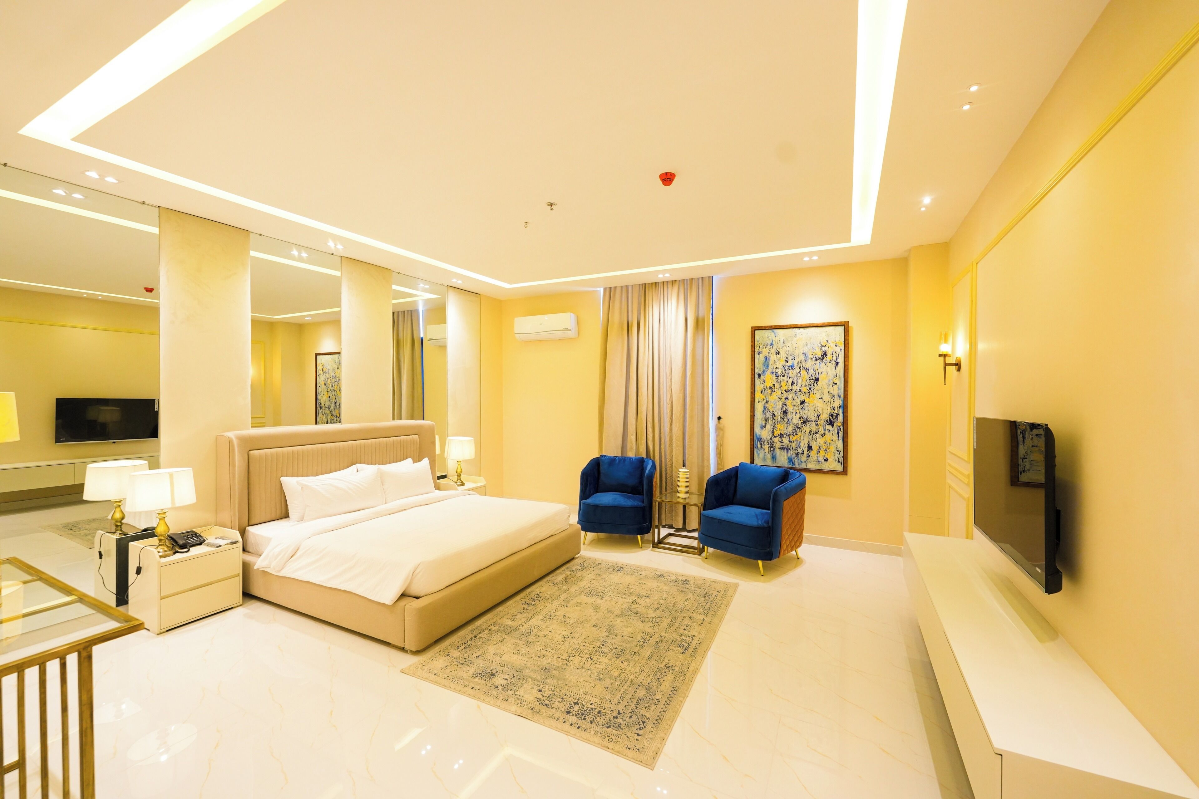 A modern hotel room with a large bed, two armchairs, a flat-screen TV, and a large mirror.